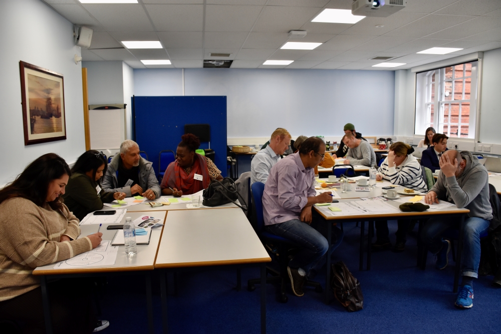 A classroom scene reveals participants immersed in a value proposition session, seated at tables, engrossed in productive discussions.
