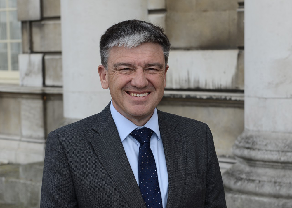 Professor Andrew Westby, former Director of NRI and current Deputy Vice-Chancellor for Research and Knowledge Exchange at the University of Greenwich, smiling outside a historic stone building